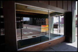 Empty storefront window with "For Sale" sign and brick base.